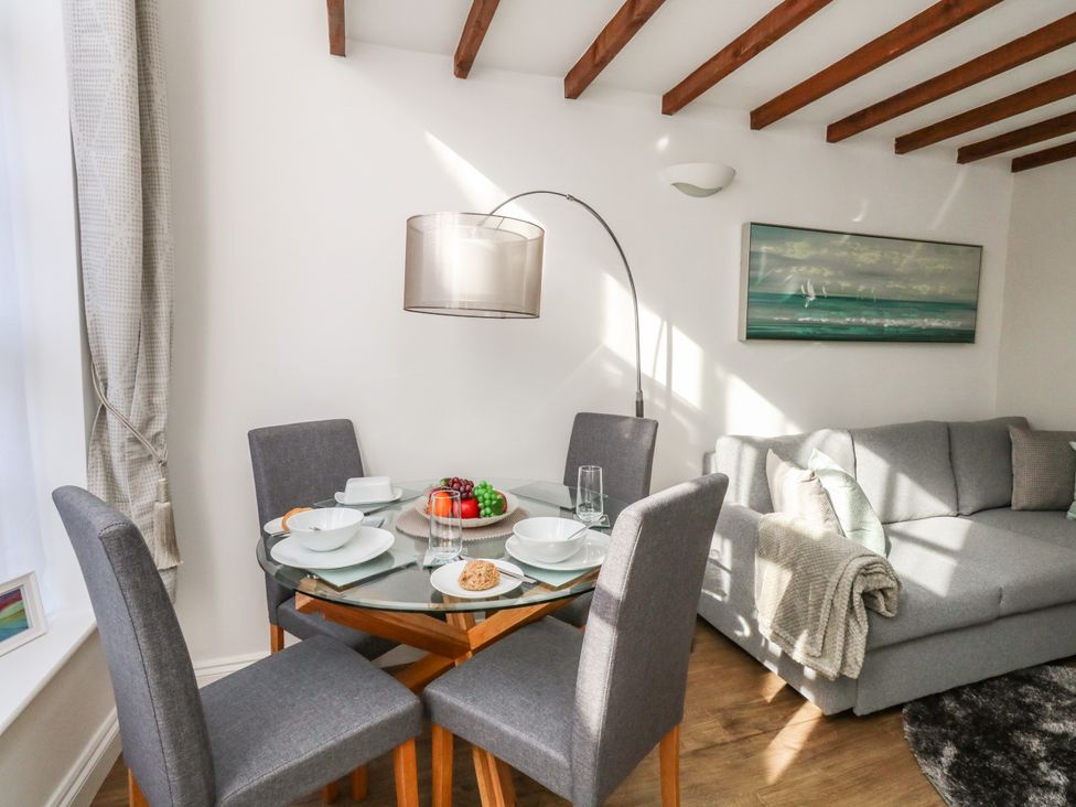 A dining area with a glass table and four chairs next to a grey sofa in a living room at Goliath in Brewers Quay Harbour
