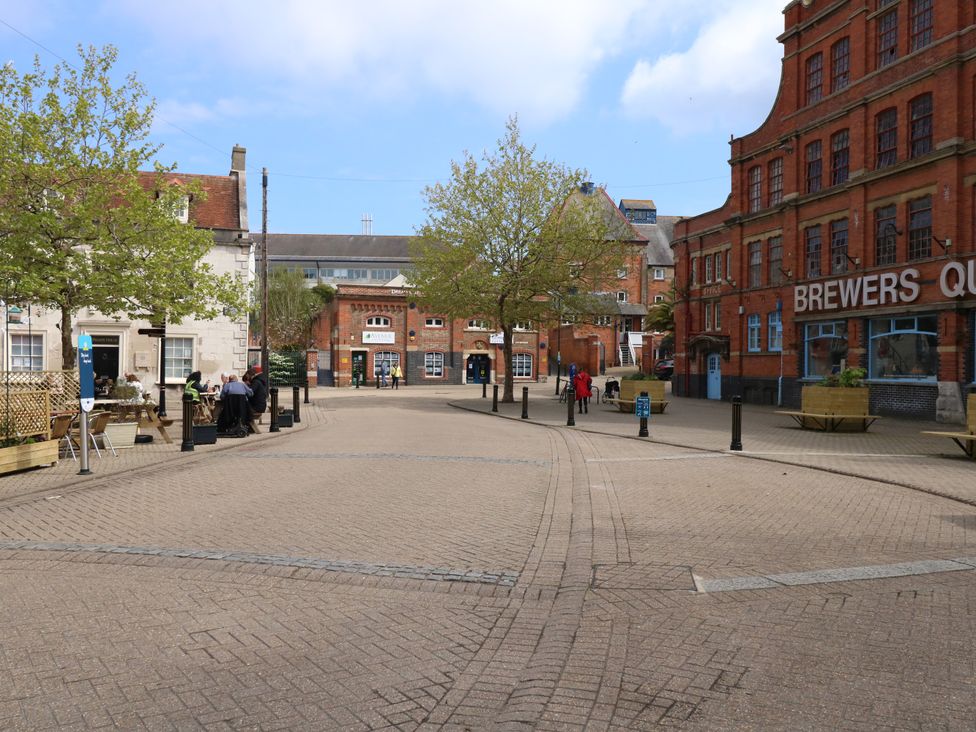 An outdoor paved public space with trees benches and people near brick buildings at Brewers Quay Harbour