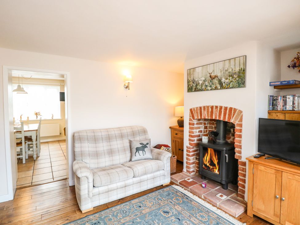 A living room with a plaid sofa and a wood burning stove in a brick fireplace at 1 Chelsea Cottage in North Elmham