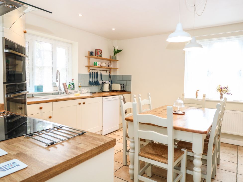 A kitchen with wooden countertops white cabinets a dining table with six chairs and kitchen appliances at 1 Chelsea Cottage in North Elmham