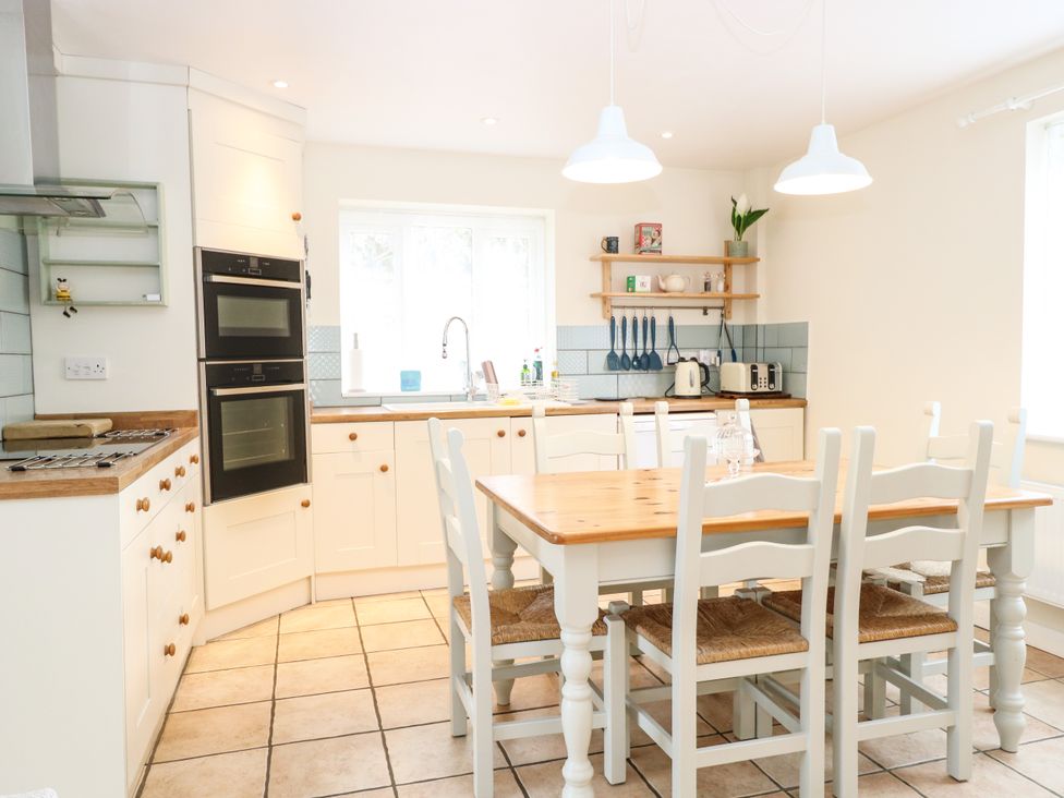 A kitchen with a wooden dining table and chairs near white cabinets and a window at 1 Chelsea Cottage in North Elmham