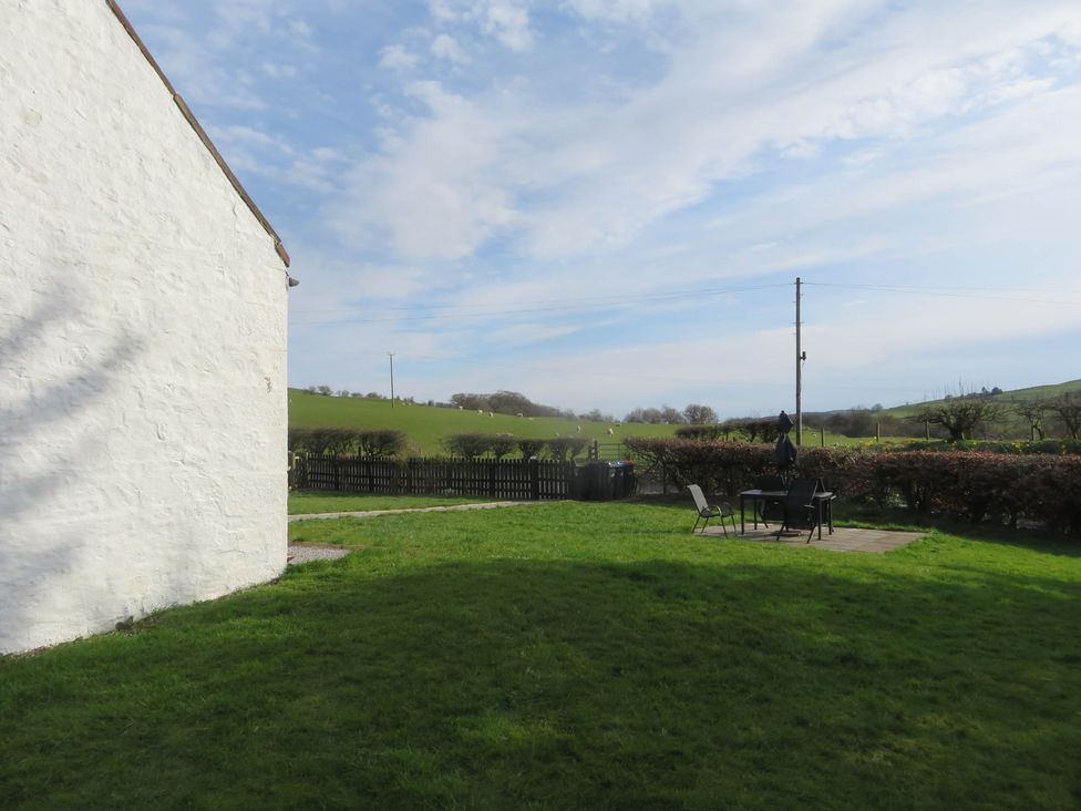 A grassy backyard with patio furniture and a white building on the left and a rural landscape beyond Marr Cottage in Thornhill