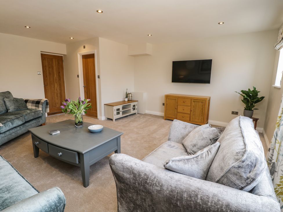 A living room with sofas a coffee table with flowers a wall-mounted TV and wooden cabinets at Rose Cottage Faceby near Swainby