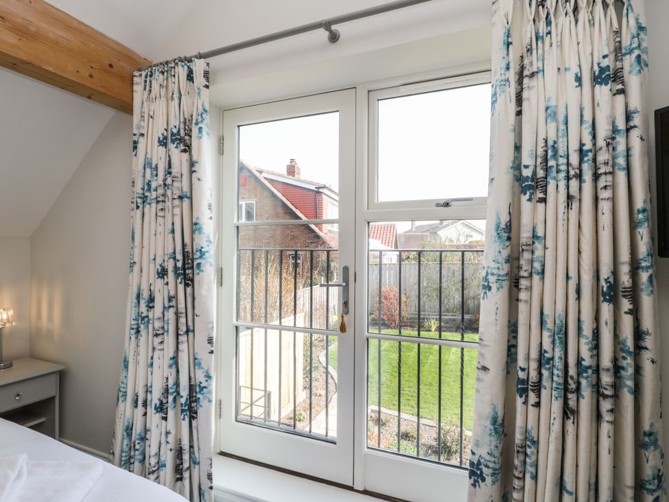 A bedroom window with blue and white curtains overlooking a garden at Rose Cottage in Faceby near Swainby