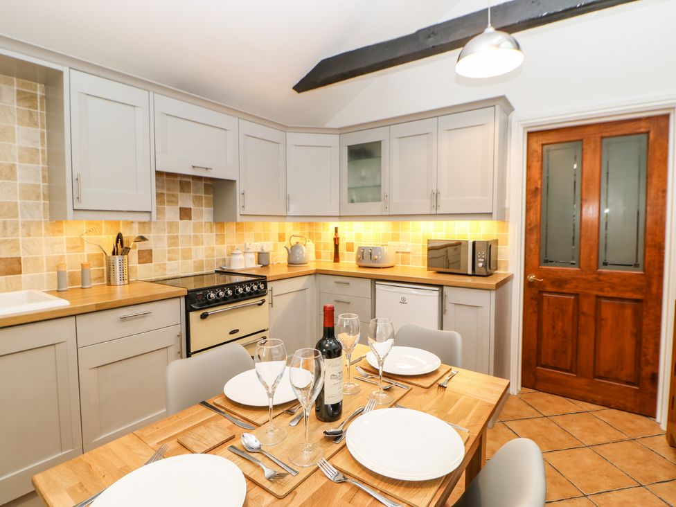 A kitchen with wooden table set for four people and light gray cabinets with tiled backsplash at Pine Cottage in Appleby-In-Westmorland