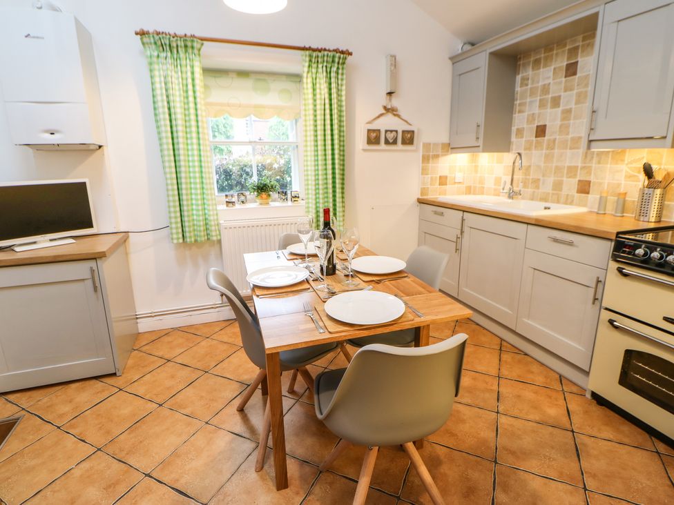 A kitchen with a wooden table set for four and green checkered curtains at Pine Cottage in Appleby-In-Westmorland