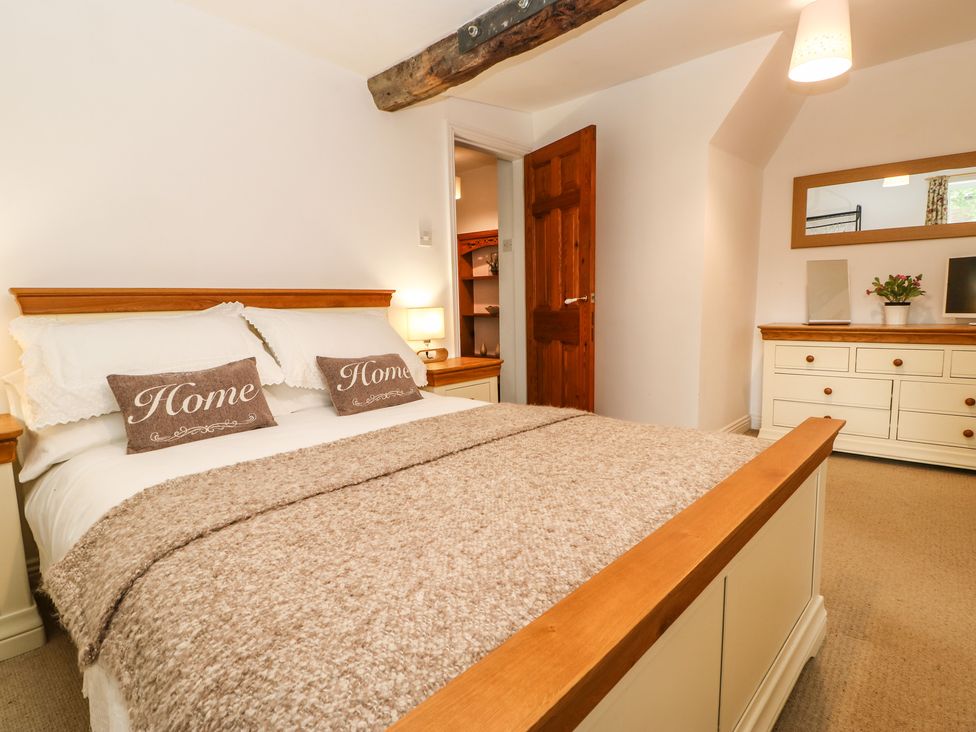 A bedroom with a wooden bed and dresser a mirror and a plant at Pine Cottage in Appleby-In-Westmorland