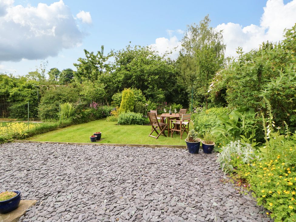 A garden with a wooden table and chairs on grass surrounded by plants and shrubs at Pine Cottage in Appleby-In-Westmorland