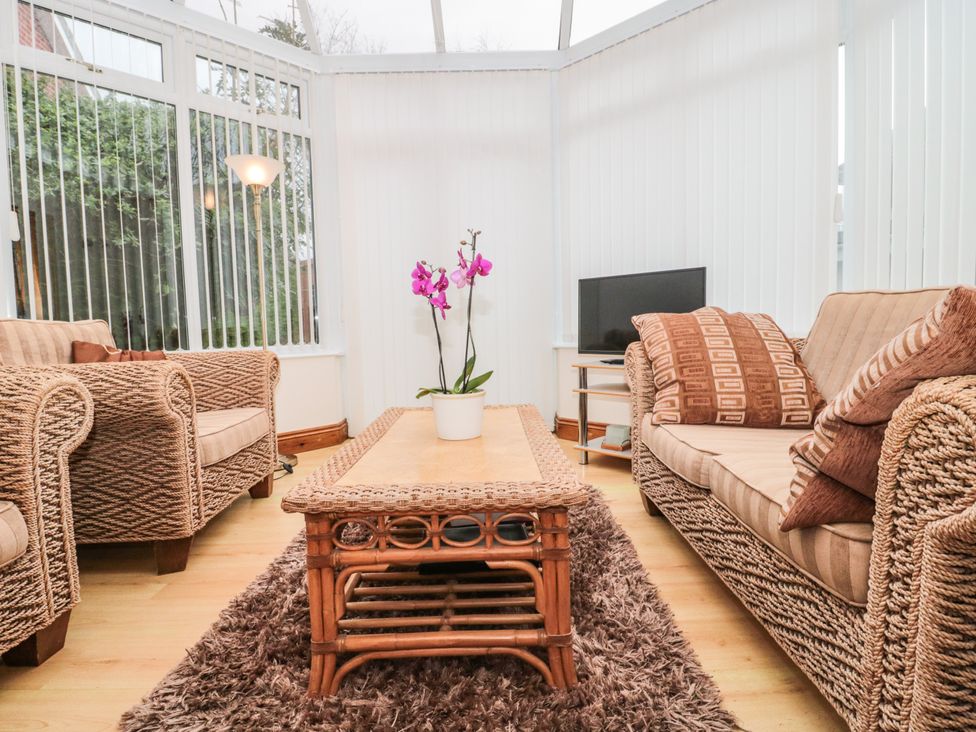 A conservatory with wicker sofas a wooden coffee table with a plant and a television on a stand at Little Walton in Burnham-On-Sea