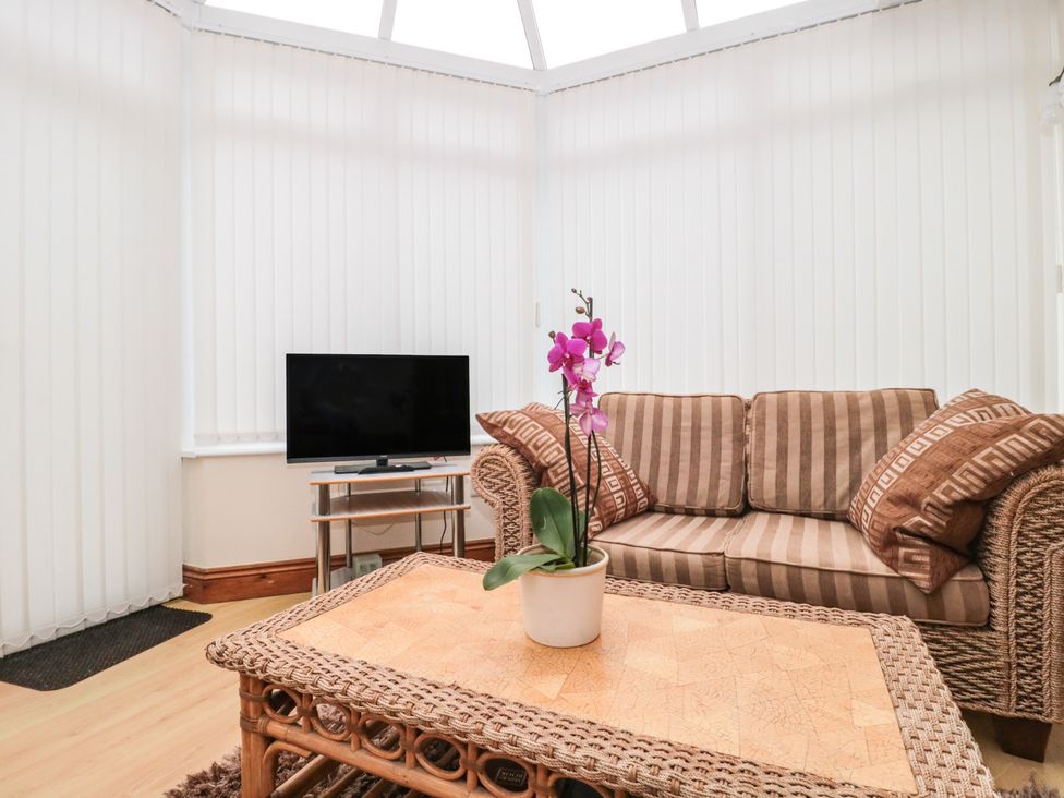 A seating area with a striped sofa a wooden coffee table with a potted orchid a small TV on a stand and vertical blinds covering the windows at Little Walton in Burnham-On-Sea