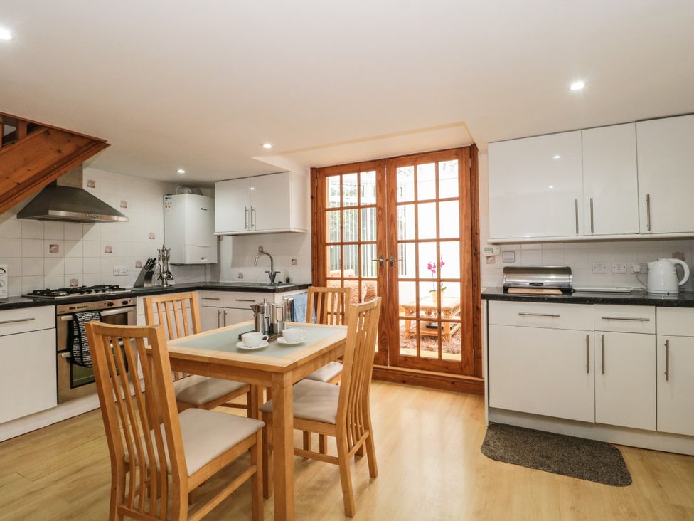 A kitchen with wooden dining table and chairs next to white cabinets and glass doors at Little Walton in Burnham-On-Sea
