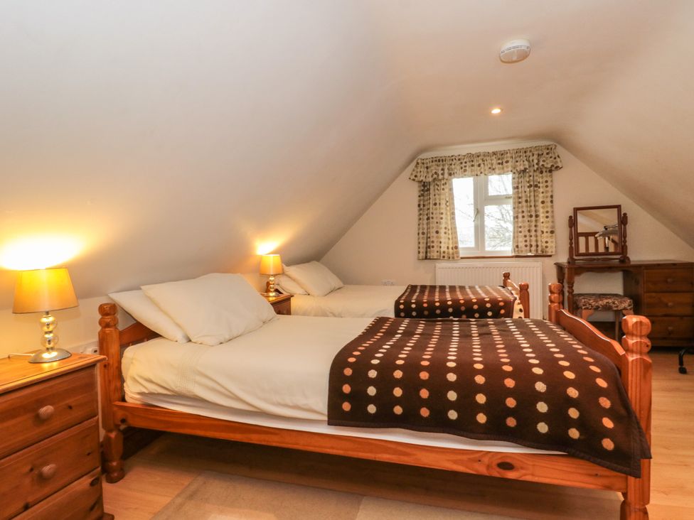A bedroom with two single wooden beds two bedside tables with lamps a window with polka dot curtains and a wooden dressing table at Little Walton Burnham-On-Sea