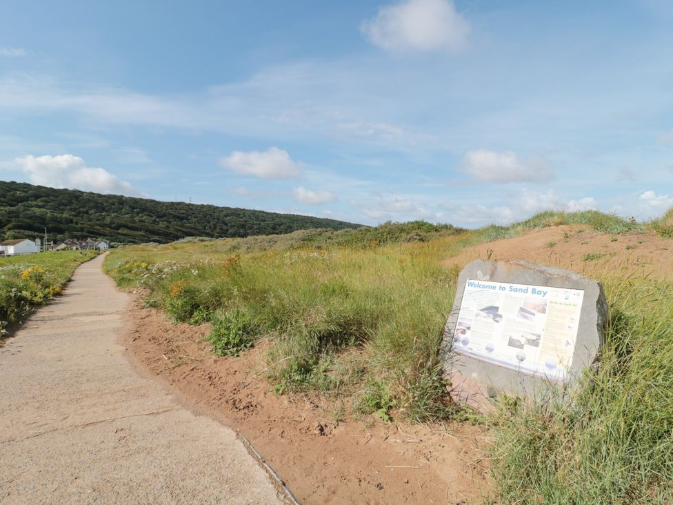 A pathway alongside grassy dunes with a welcome sign to Sand Bay in the foreground and houses in the distance at Little Walton in Burnham-On-Sea