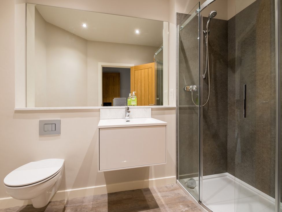 A bathroom with a wall-mounted toilet a floating sink and a glass enclosed shower at Howe Keld 5 First Floor in Keswick