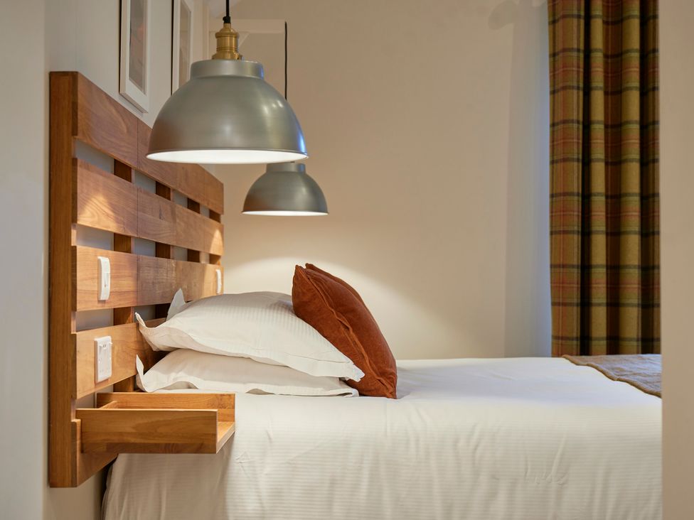 A bedroom with a wooden headboard bed white bedding two pillows and hanging pendant lights at Howe Keld 5 First Floor in Keswick