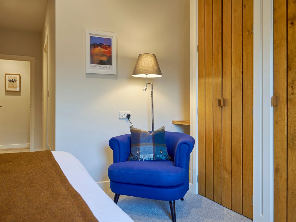 A bedroom corner with a blue armchair and brown plaid cushion next to a floor lamp and wooden closet doors at Howe Keld 5 First Floor in Keswick