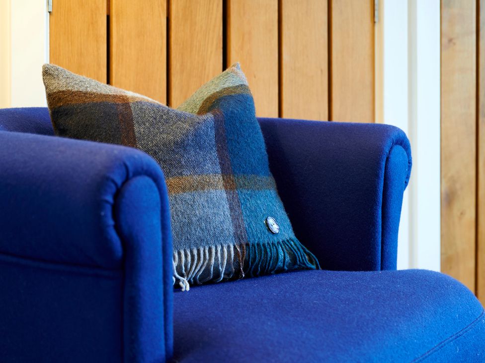 A blue armchair with a plaid cushion against a wooden panel at Howe Keld 5 First Floor in Keswick