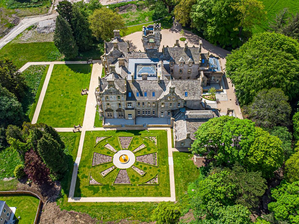 A large stone mansion with symmetrical gardens and paved pathways surrounded by trees at The Mabel Suite Stone Cross Mansion in Ulverston