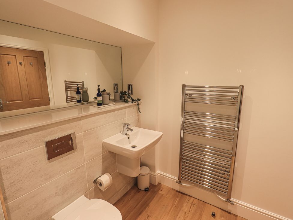 A bathroom with a sink a toilet a wall-mounted mirror and a chrome towel radiator at The Mabel Suite Stone Cross Mansion in Ulverston