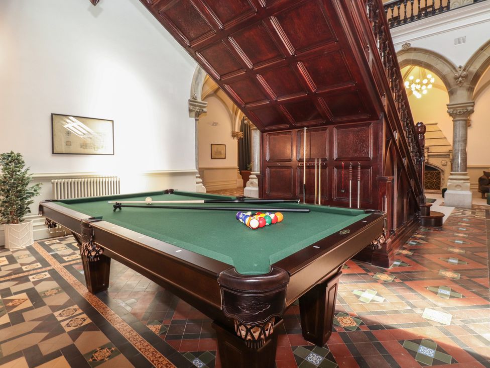 A billiard table with pool cues and balls under a wooden staircase in a tiled room at The Mabel Suite Stone Cross Mansion in Ulverston
