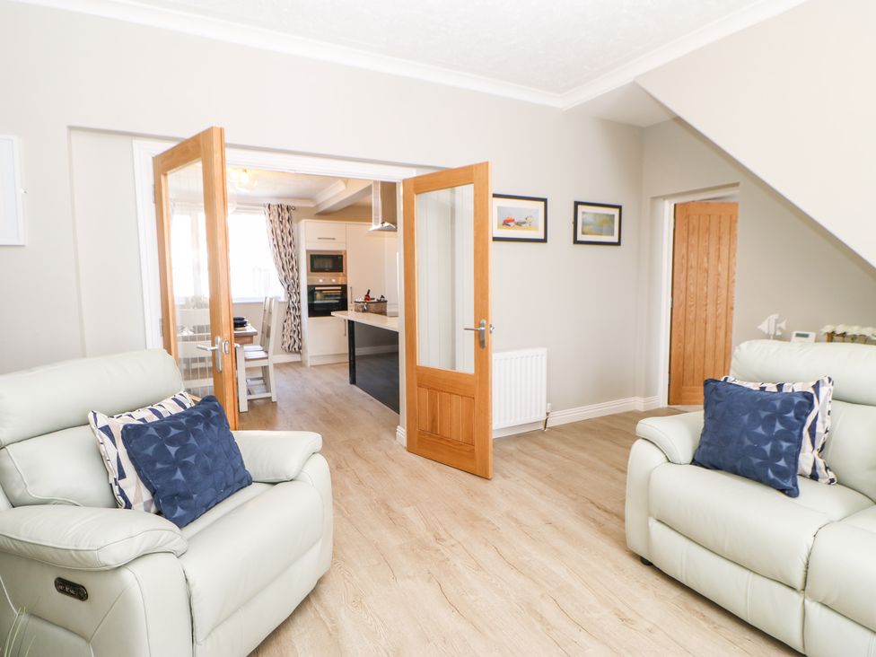 A living room with two armchairs and open wooden doors leading to a kitchen at Lobster Pot Retreat in Newbiggin-By-The-Sea