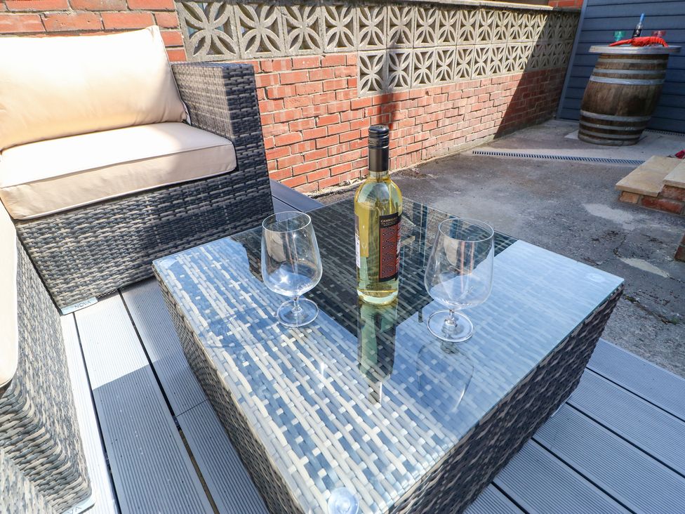An outdoor seating area with a wicker sofa and glass table with a bottle and two glasses at Lobster Pot Retreat in Newbiggin-By-The-Sea
