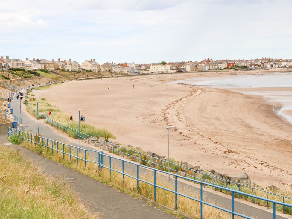 A view of a sandy beach with a walkway and railings along the side and houses in the background at Lobster Pot Retreat in Newbiggin-By-The-Sea