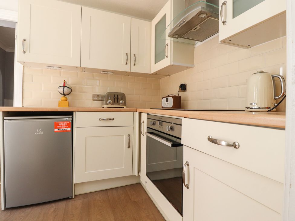A kitchen with white cabinets a silver mini fridge a toaster an oven a kettle and a wooden countertop at The Mews Cottage in Lytham St Annes