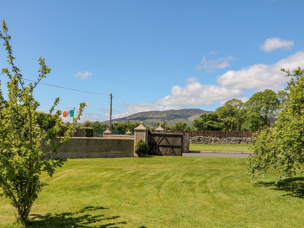 A garden with green grass and small trees with a stone wall fence and mountains in the background at Willow Tree Farm House in Newry near Jonesborough