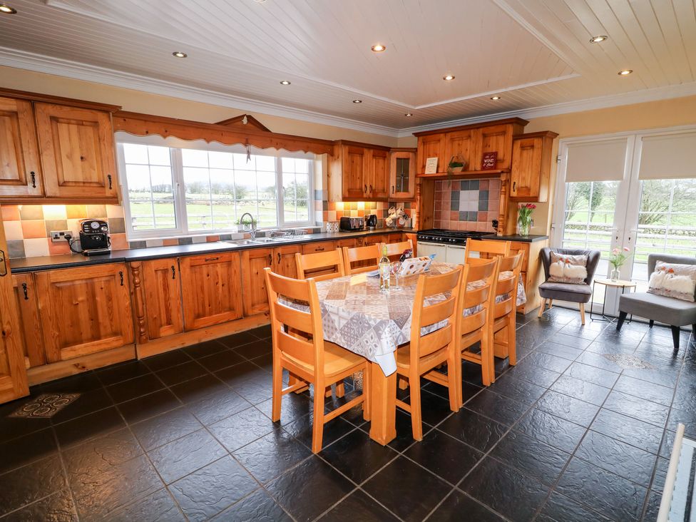 A kitchen with wooden cabinets a central dining table with chairs and windows overlooking a grassy area at Willow Tree Farm House in Newry near Jonesborough