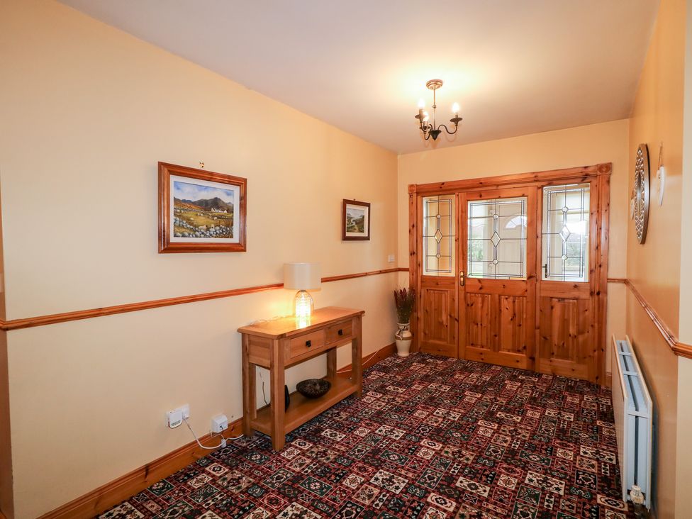 An entrance hallway with wooden double doors a wooden console table with a lamp paintings on walls and a patterned carpet at Willow Tree Farm House in Newry near Jonesborough