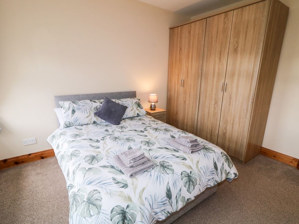A bedroom with a bed with leafy patterned bedding bedside table with lamp and wooden wardrobe at Willow Tree Farm House in Newry near Jonesborough