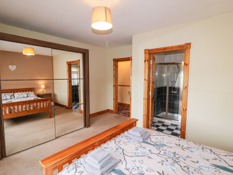 A bedroom with a wooden bed and floral bedding a mirrored wardrobe an open door leading to a bathroom with a shower at Willow Tree Farm House in Newry near Jonesborough
