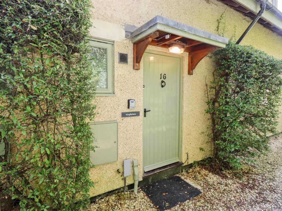 A green front door with number 16 and small canopy surrounded by bushes at Kingfisher House in Cotswold Water Park