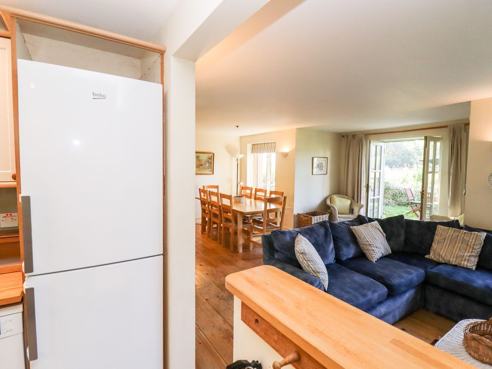 A kitchen with white refrigerator next to a living room with blue sofa and dining table at Kingfisher House in Cotswold Water Park