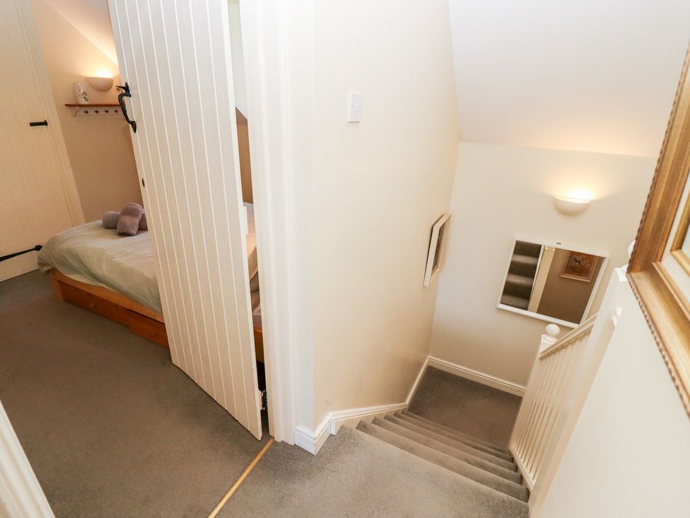 A staircase with grey carpet leading down beside a small bedroom with a bed and folded towels at Kingfisher House in Cotswold Water Park