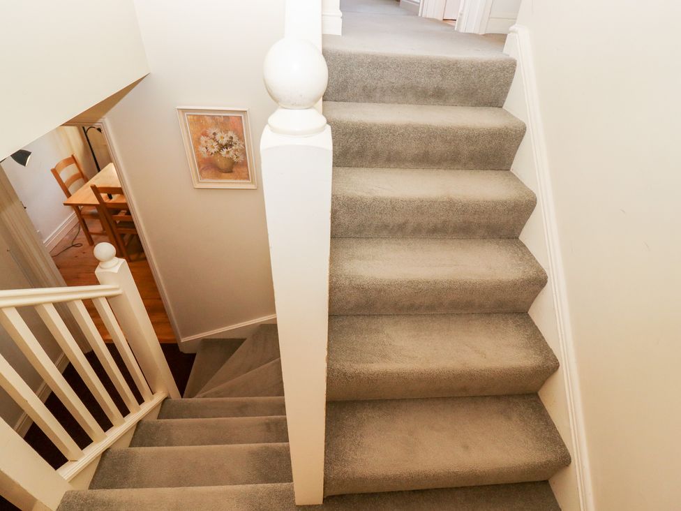 A carpeted staircase with white railings leading to a room with a wooden table and chairs at Kingfisher House in Cotswold Water Park
