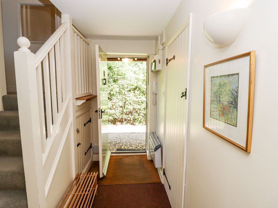 A hallway with stairs, a wooden shoe rack, an open door leading outside, and a framed picture on the wall at Kingfisher House in Cotswold Water Park
