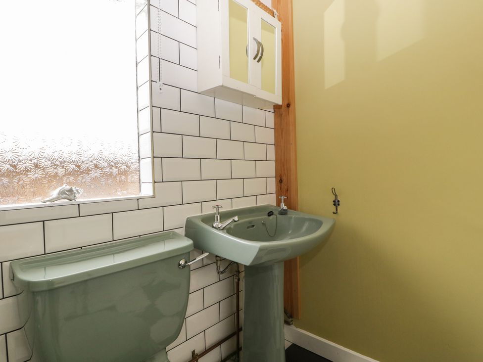 A bathroom with a green toilet and sink white tiled wall and yellow painted wall at Lulu Logs in Congresbury