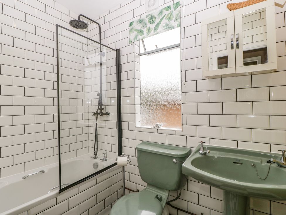 A bathroom with a green toilet and sink a bathtub with a shower and tiled walls at Lulu Logs in Congresbury