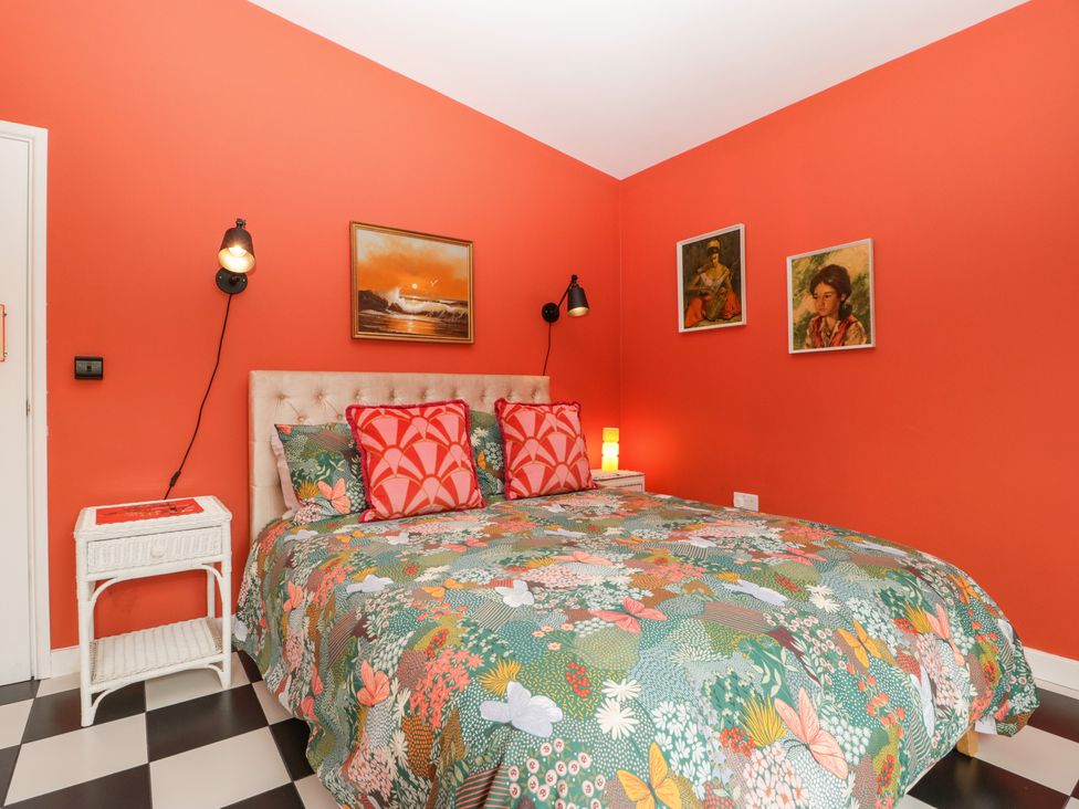 A bedroom with an orange wall a bed with floral and butterfly bedding and two white bedside tables at Lulu Logs in Congresbury