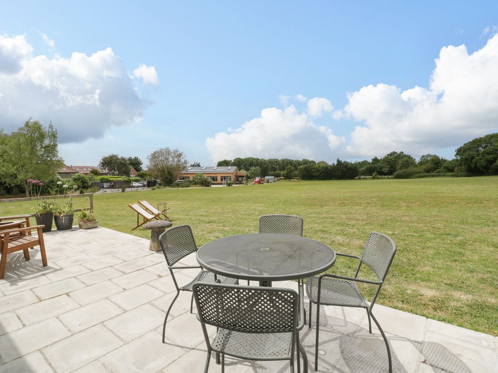 A patio with a round metal table and four chairs overlooking a large grassy field at Lulu Logs in Congresbury