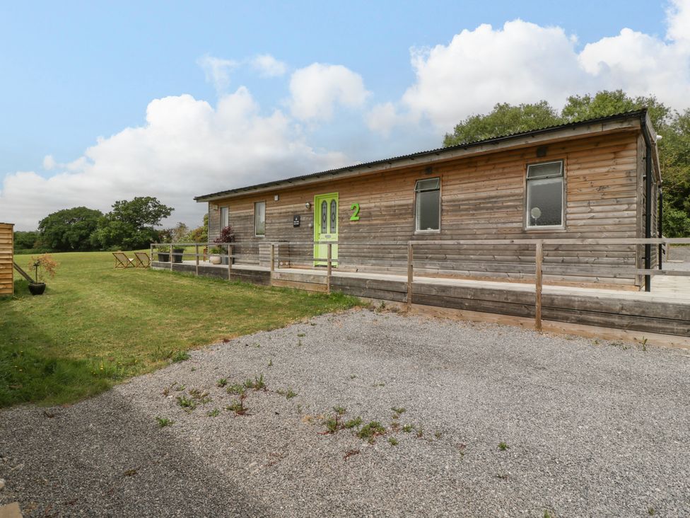 A wooden cabin with a green door and gravel driveway next to a grassy field at Lulu Logs in Congresbury