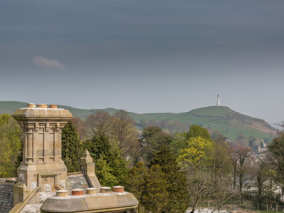A view of stone chimneys with trees and a hill with a monument in the background at The Margaret Suite Stone Cross Mansion in Ulverston