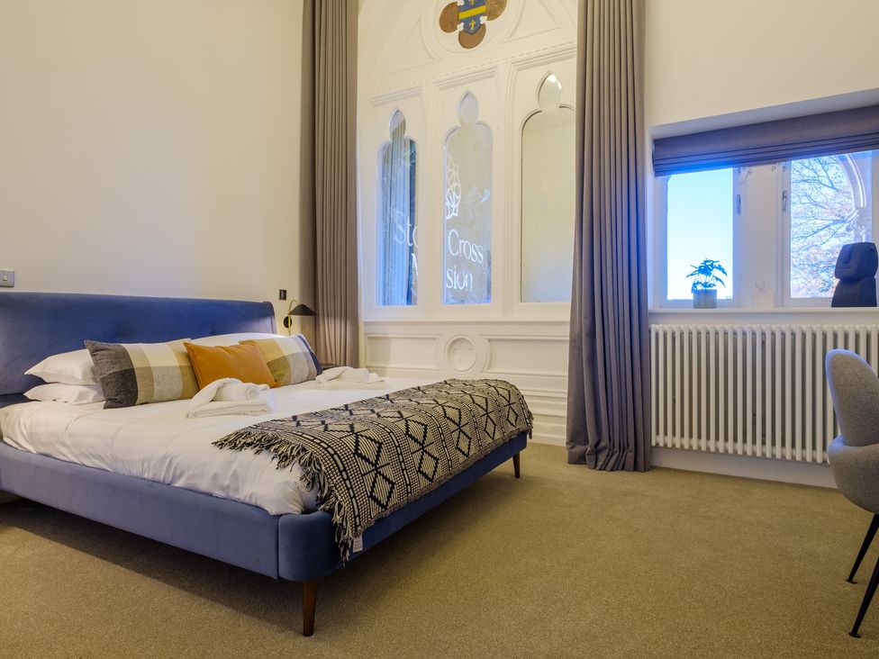 A bedroom with a blue bed and decorative pillows next to windows with curtains at The Margaret Suite Stone Cross Mansion in Ulverston