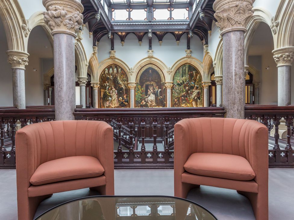 A seating area with two armchairs and a glass table in a hall with columns and arched artwork at The Violet Suite Stone Cross Mansion in Ulverston