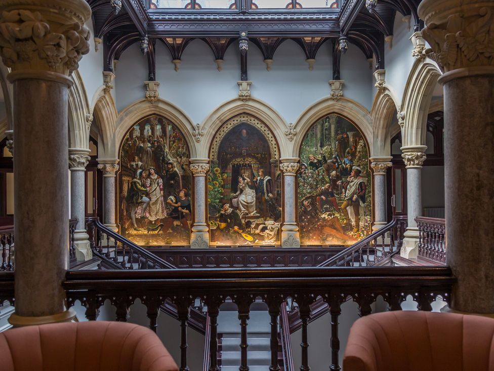 A hallway with arched columns and three large paintings above a wooden staircase at The Violet Suite Stone Cross Mansion in Ulverston