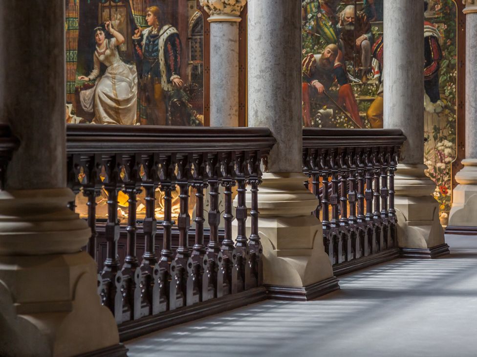 A hallway with stone columns and wooden railing with paintings in the background at The Violet Suite Stone Cross Mansion in Ulverston