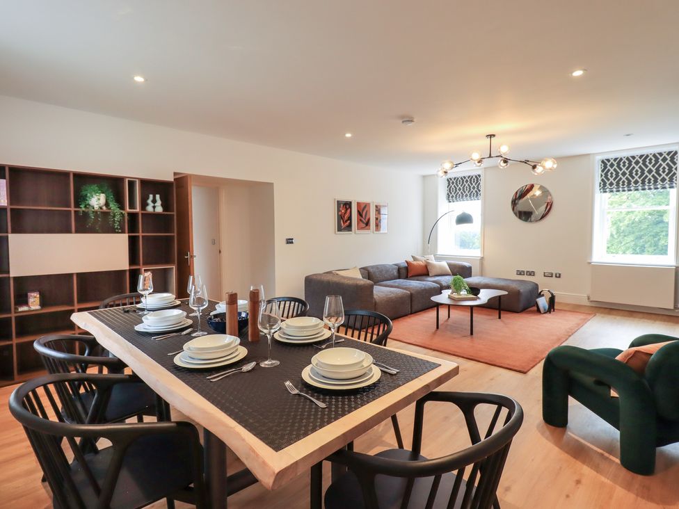 A dining table set with plates and glasses beside a living area with a gray sofa and orange rug at The Violet Suite Stone Cross Mansion in Ulverston
