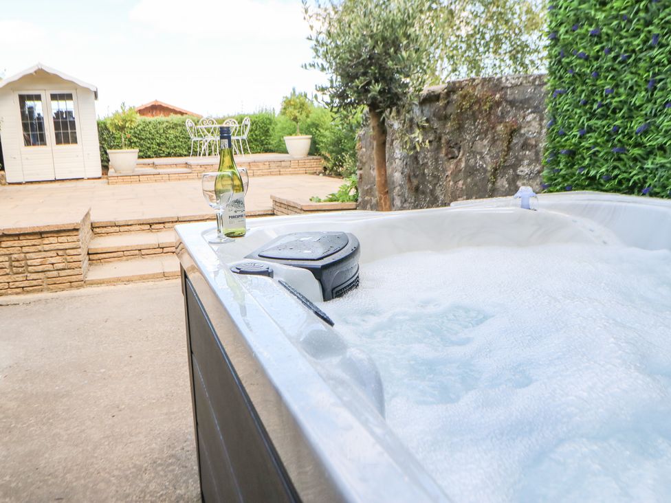 An outdoor hot tub with a bottle of wine and two glasses patio steps a small white shed and garden furniture at Dale Cottage in Ingleton County Durham